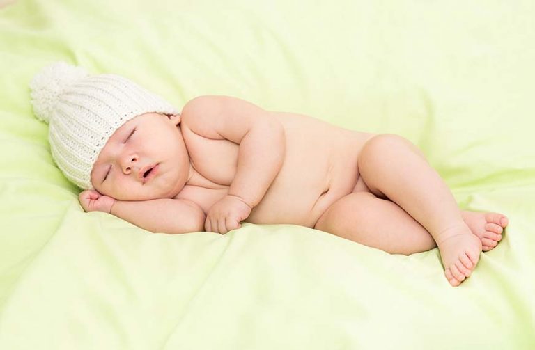 תינוקת ישנה, ערומה על שמיכה ירוקה עם כבוע לבן
