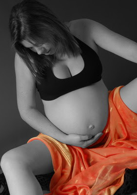 אישה בהריון יושבת ומחזיקה את הבטן החשופה שלה