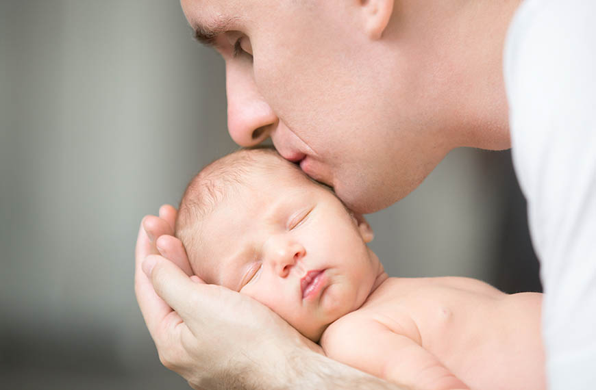 אבא מחזיק בידיו תינוק ערום ומנשק את פניו