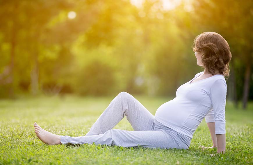 אשה בהריון יושבת על הדשא ונשענת לאחור