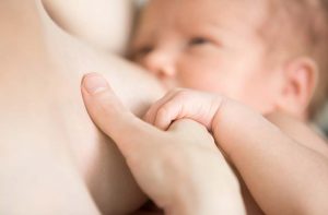 תינוק יונק מחזיק את היד של אמא