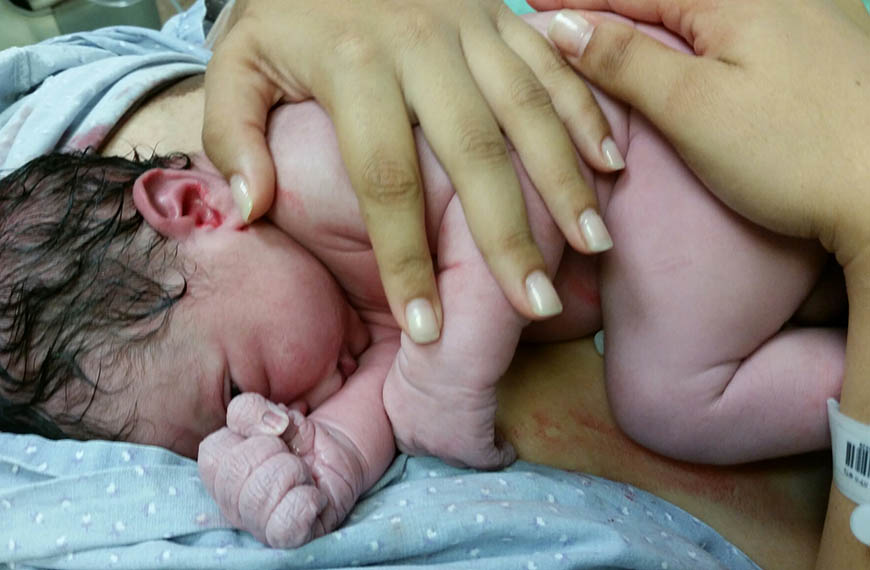 תינוק טרי שוכב על הצד ויד של אמא מחזיקה אותו