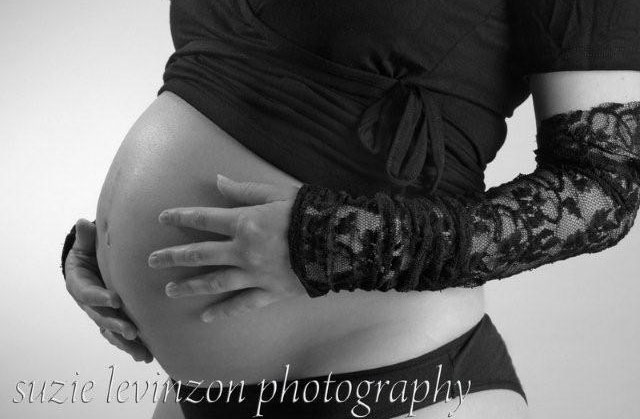 אשה בהריון עומדת על הצד עם ידיים על הבטן