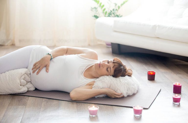 Pregnant woman relaxing after yoga practice in corpse pose at ho