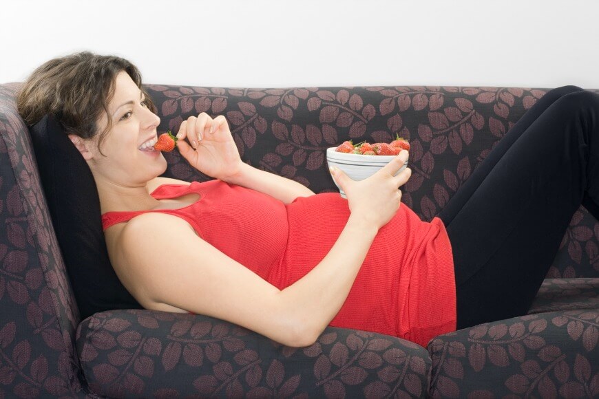 Pregnant woman eating strawberries on sofa