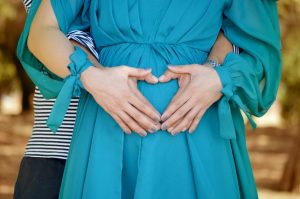 art shaped hands on a pregnant belly in blue dress