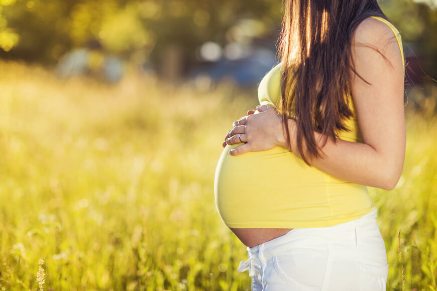 אשה בהריון בחולצה צהובה על רקע דשא